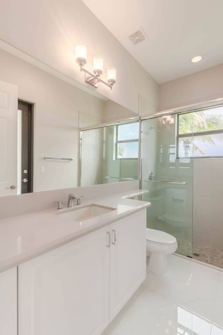 Bathroom with glass sliding doors, shower, white flooring, and Formica countertops