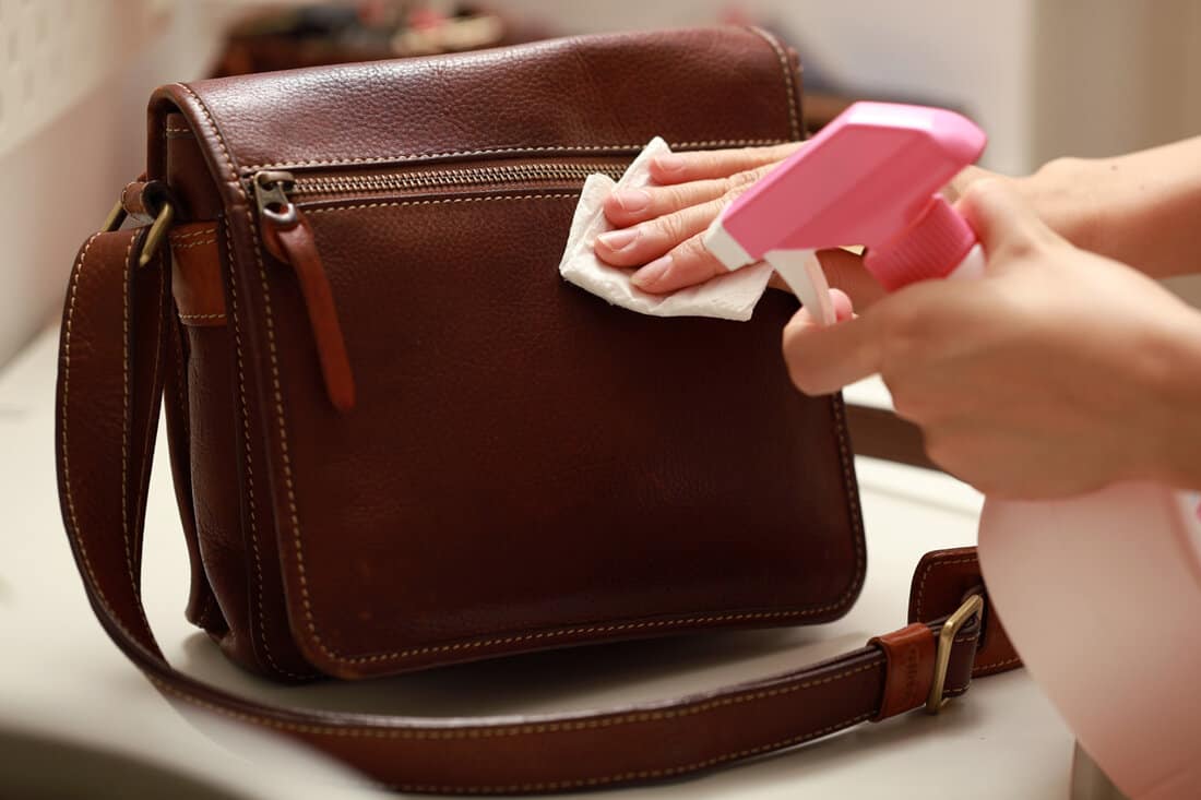 Female hand cleaning the surface of the leather bag.