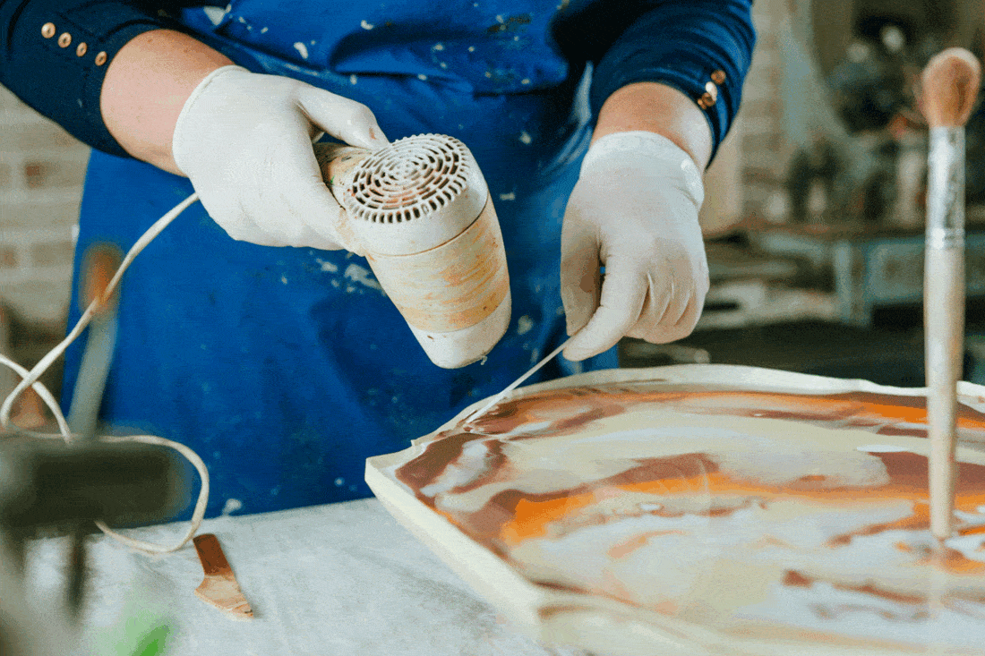 Woman wearing rubber gloves using hair dryer for liquid resin with pigments