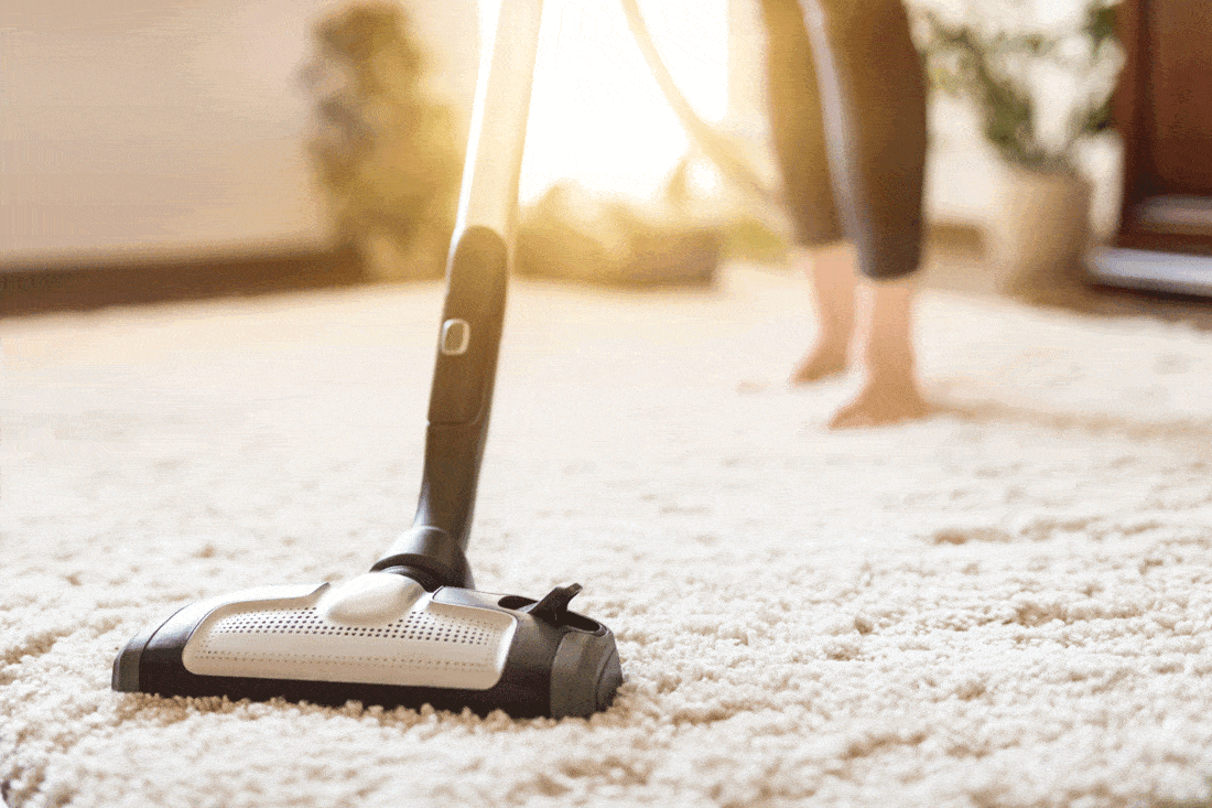 Young-woman-using-a-vacuum-cleaner-while cleaning carpet in the house