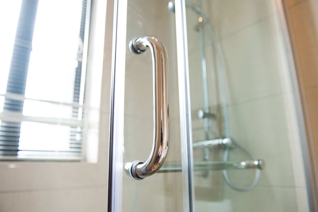 A stainless steel shower door handle photographed in great detail