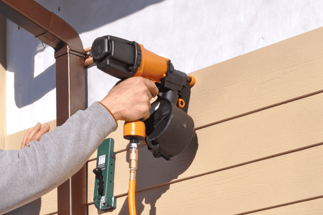 Man installing fibrous cement siding with nail gun