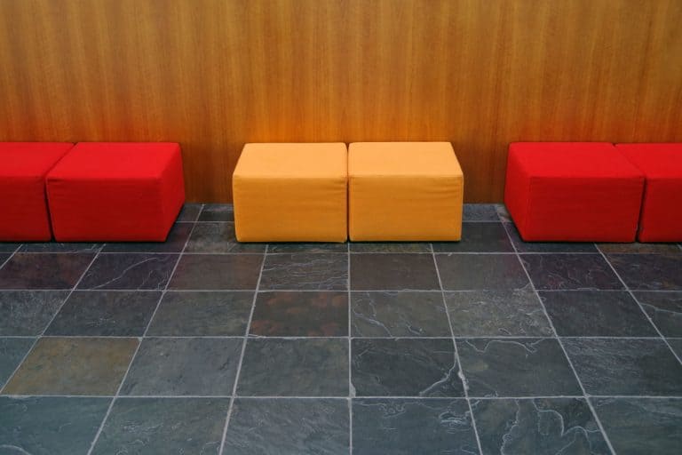 Red and yellow colored chairs inside a modern living room with slate tiles and a laminated wall, Slate vs. Porcelain Tiles: The Pros, Cons, and Differences - Your Ultimate Guide to Choosing the Perfect Flooring