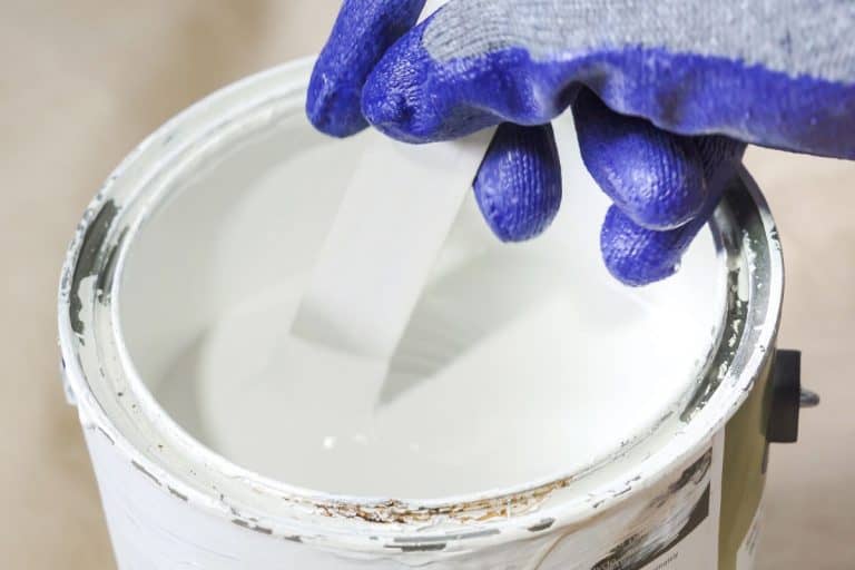 Close up of hand gloved painter mixing paint in metal paint can with wooden stick