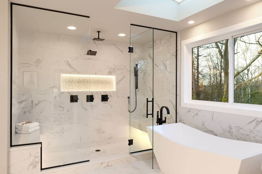 Detailes of the larhe walk in shower with white marble and mosaic light Three handles shower head in dark brass and free standing modern tub
