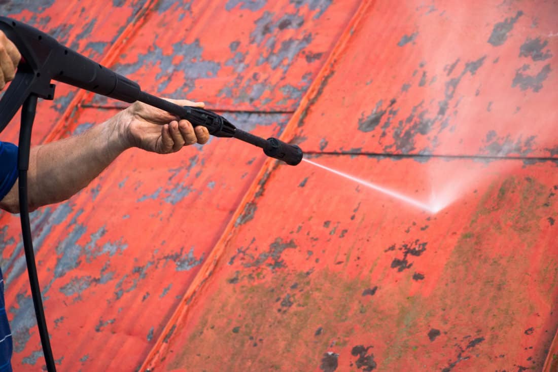 Man is washing metal roof with a high pressure washer