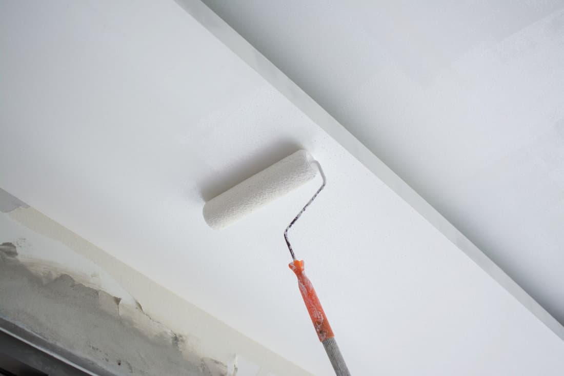 Roller brush painting a white ceiling