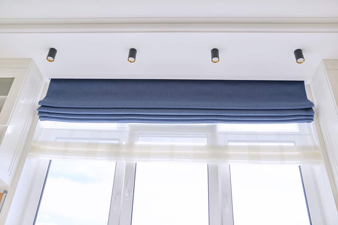 Roman blind in the interior detail close-up. Curtain blue blackout fabric, sheers white linen, fashionable modern window decoration design at home
