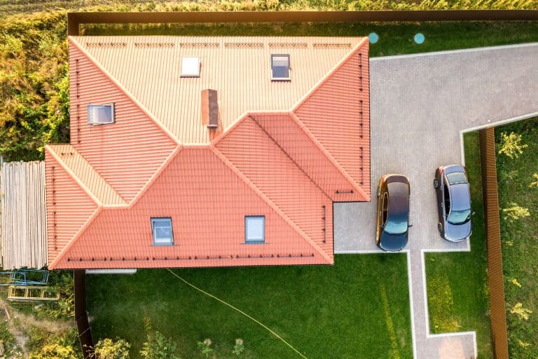 Top down aerial view of a private house with red tiled roof and spacious yard with parked two new cars.