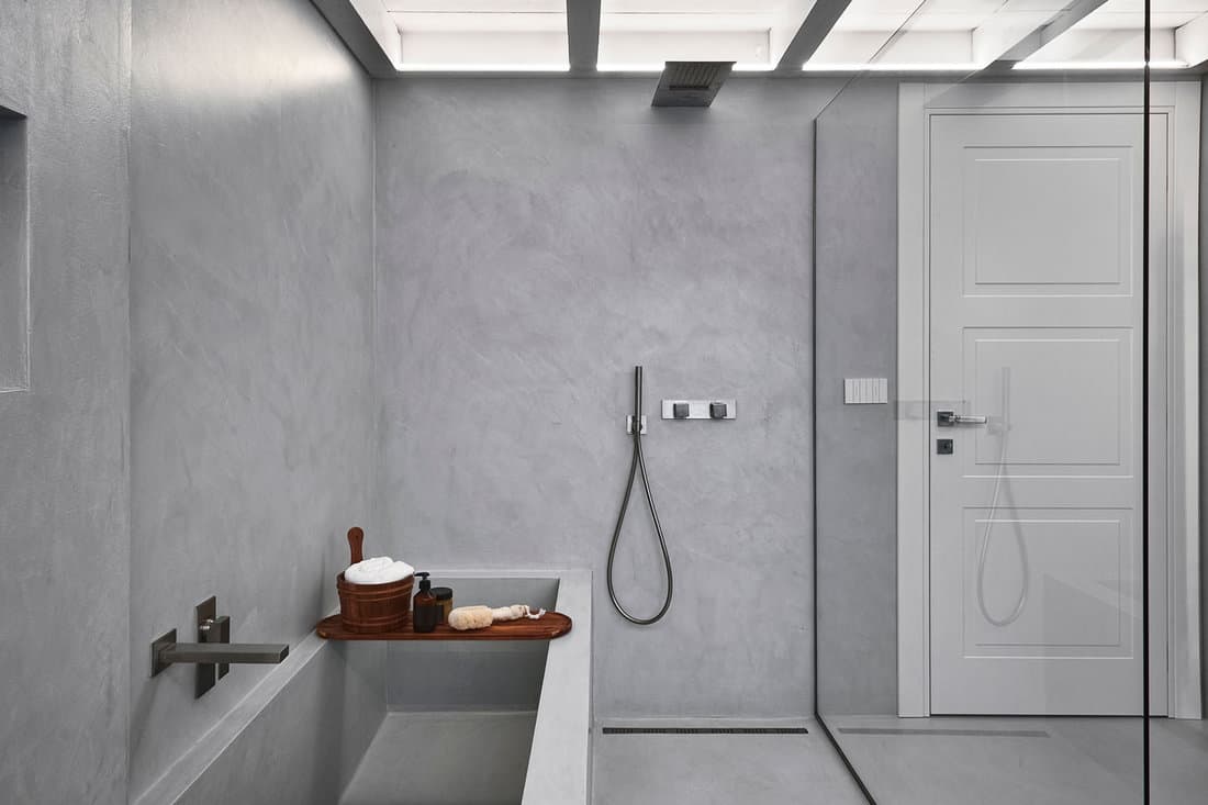 interior of a modern bathroom, in the foreground the masonry shower box and the tub the all covered in grey resin
