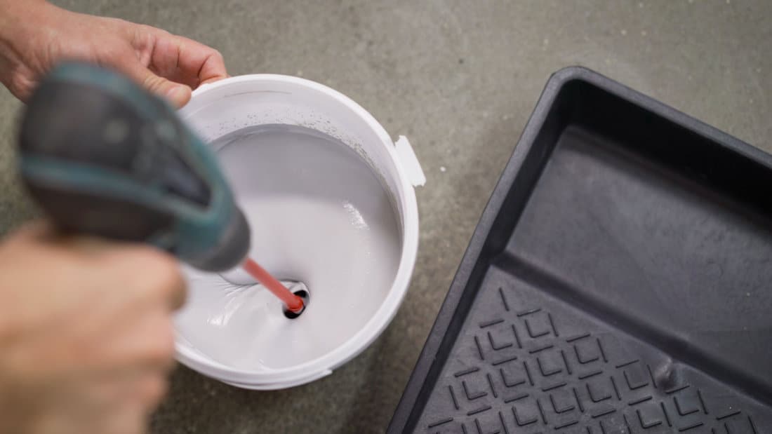 white paint is mixed in a bucket with a drill