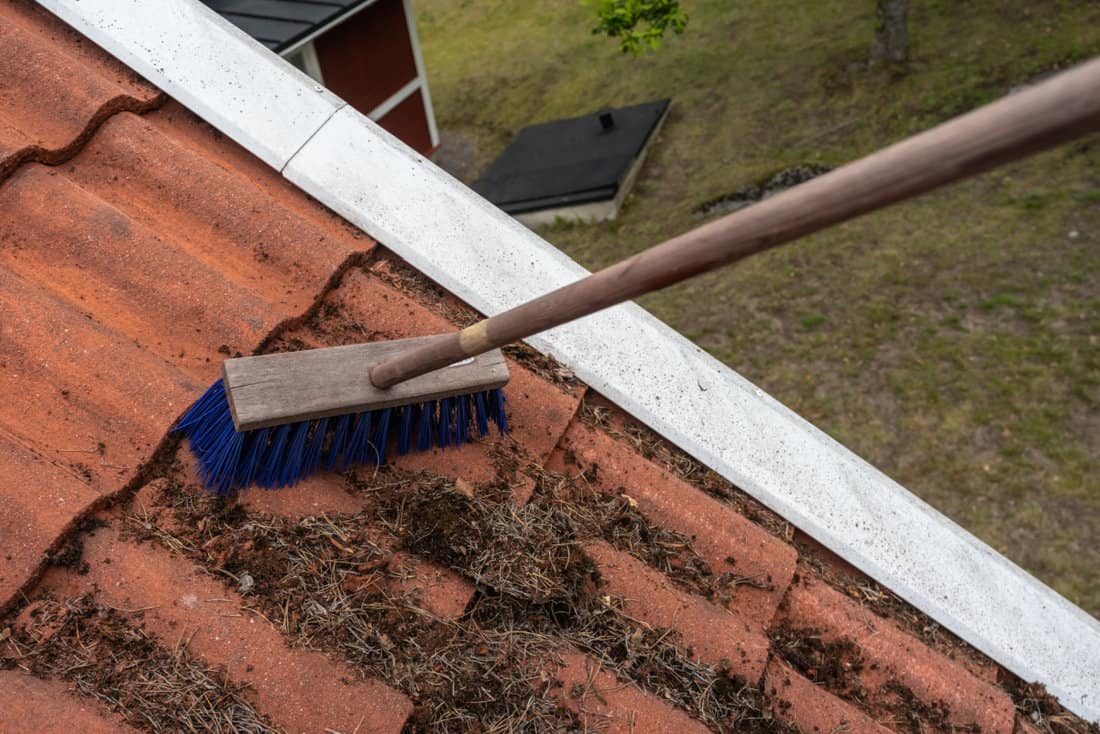 workers clean tiled roof from dirt with special brushes