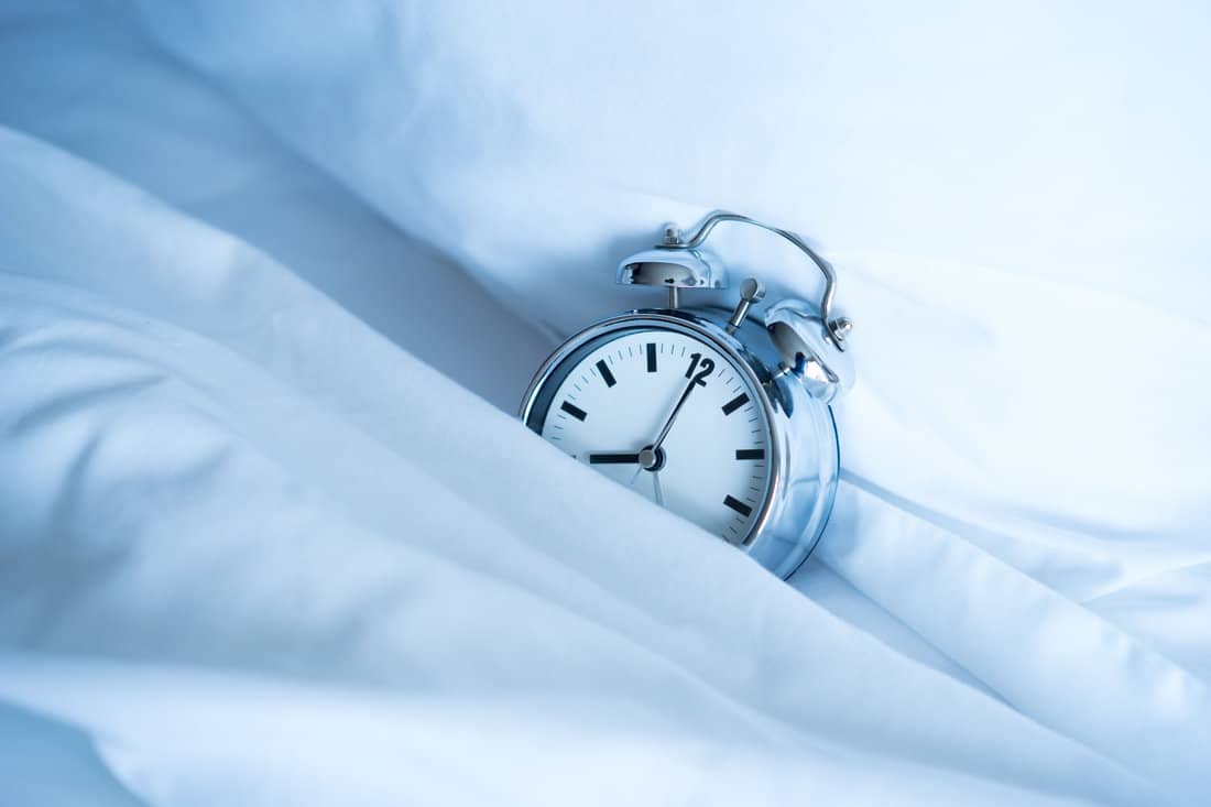 alarm clock in white bed sheets