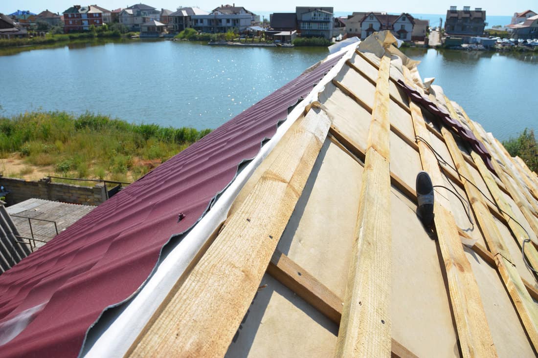A close-up on an unfinished roof ridge with a vapor, moisture barrier and Lightweight Metal Roofing Sheets installed over a roofing deck, sheathing.

