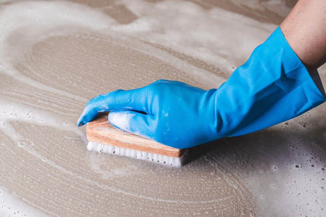 A man wearing blue rubber gloves is scrubbing tiles soaked in muriatic acid