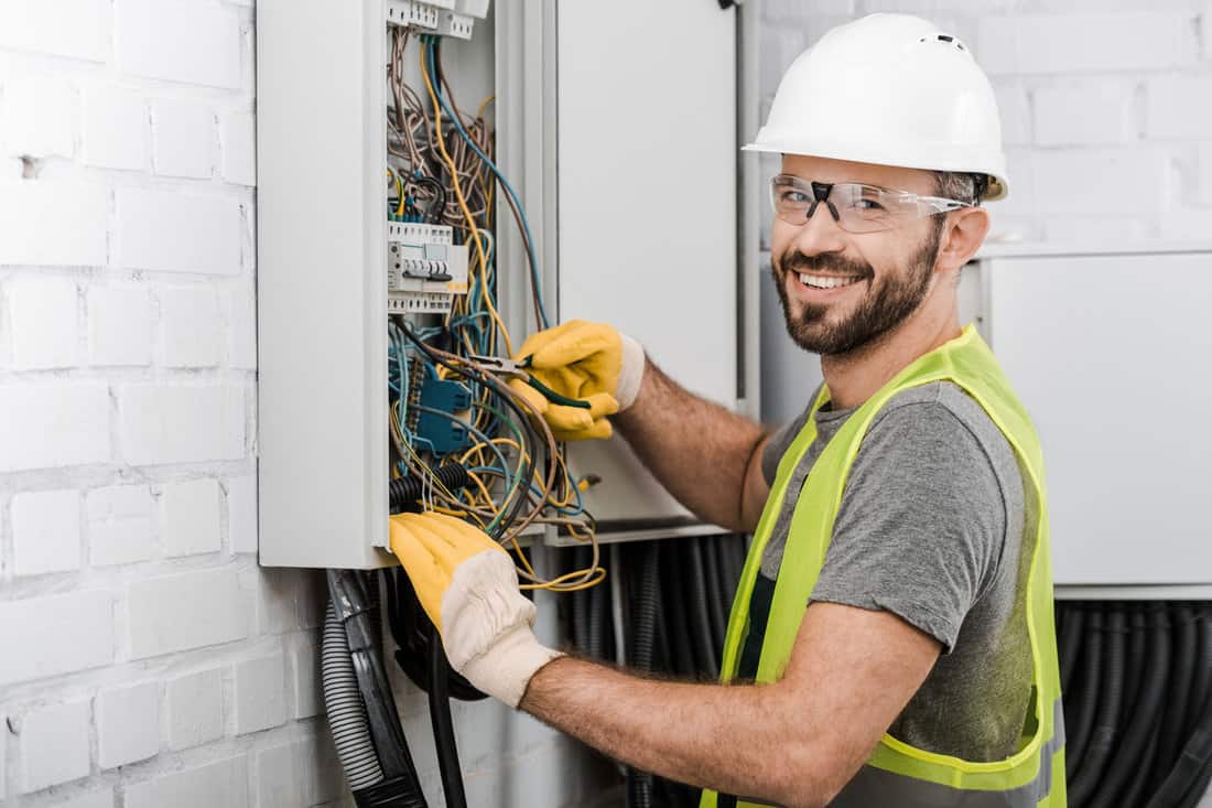 A smiling, handsome electrician is preparing the electrical box for doorbell repair.