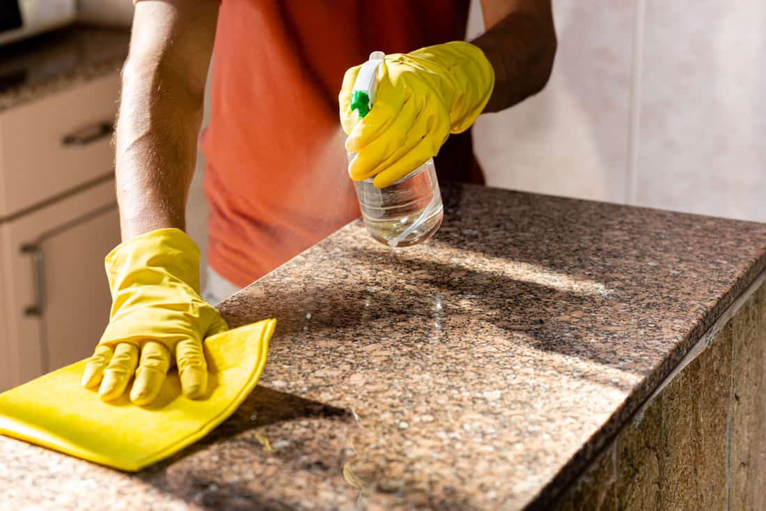 A woman is applying granite sealer onto her gleaming kitchen countertops.

