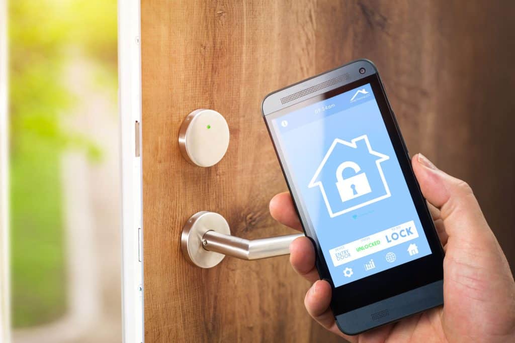 In a smart home setting, amidst home automation devices and app icons, a man employs his smartphone with a smart home security app to effortlessly unlock the door of his house.