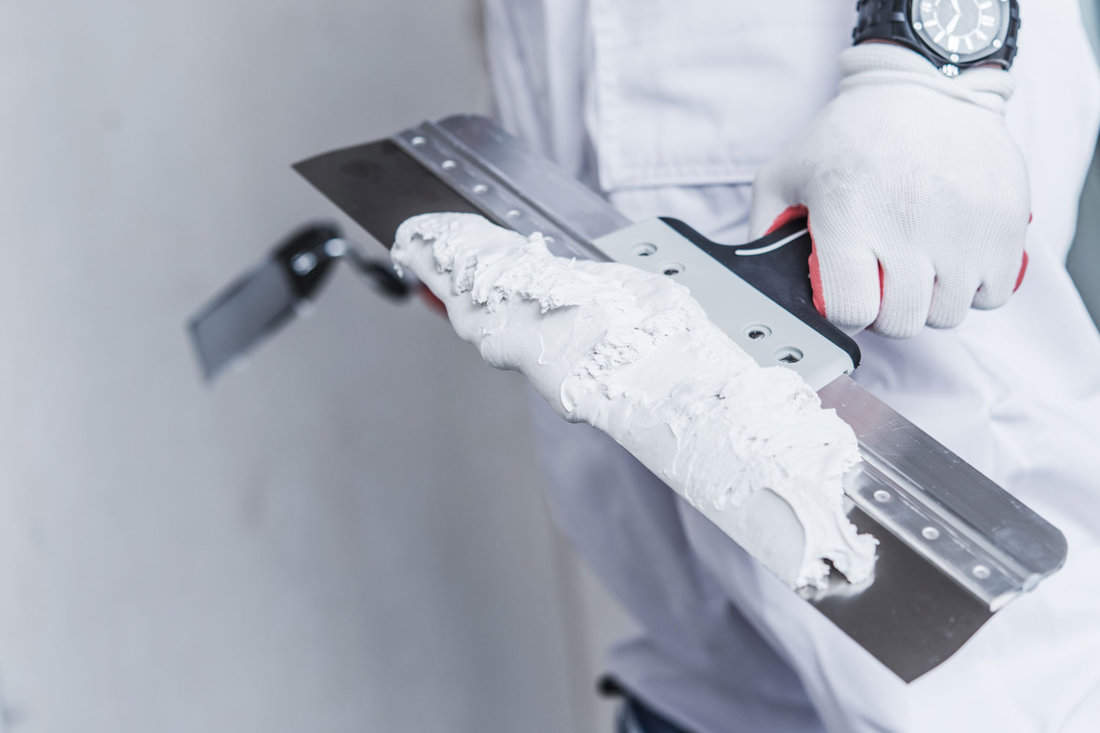 In a closeup photo, a worker with patching tools in hand prepares for drywall patching, utilizing joint compound material.
