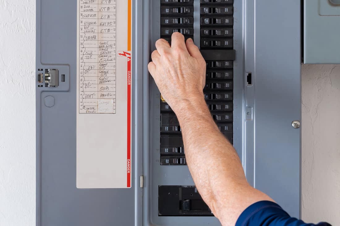 Male electrician turning off power for doorbell at circuit breaker box.