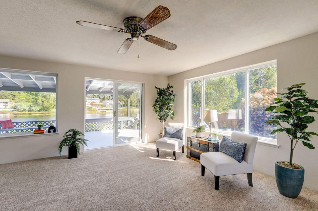Older midcentury rambler interior with white ceiling and beige carpet, sofa, chairs and lake view.
