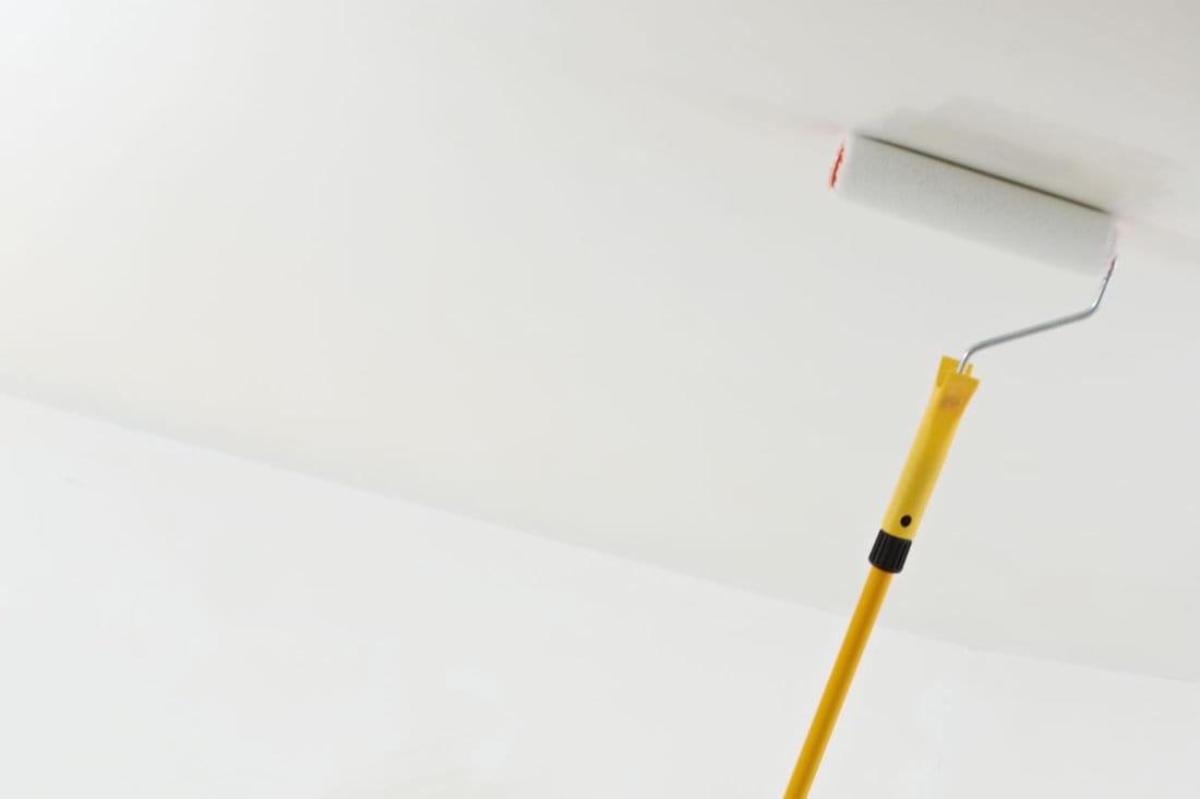 One male house painter worker painting and priming ceiling with painting roller
