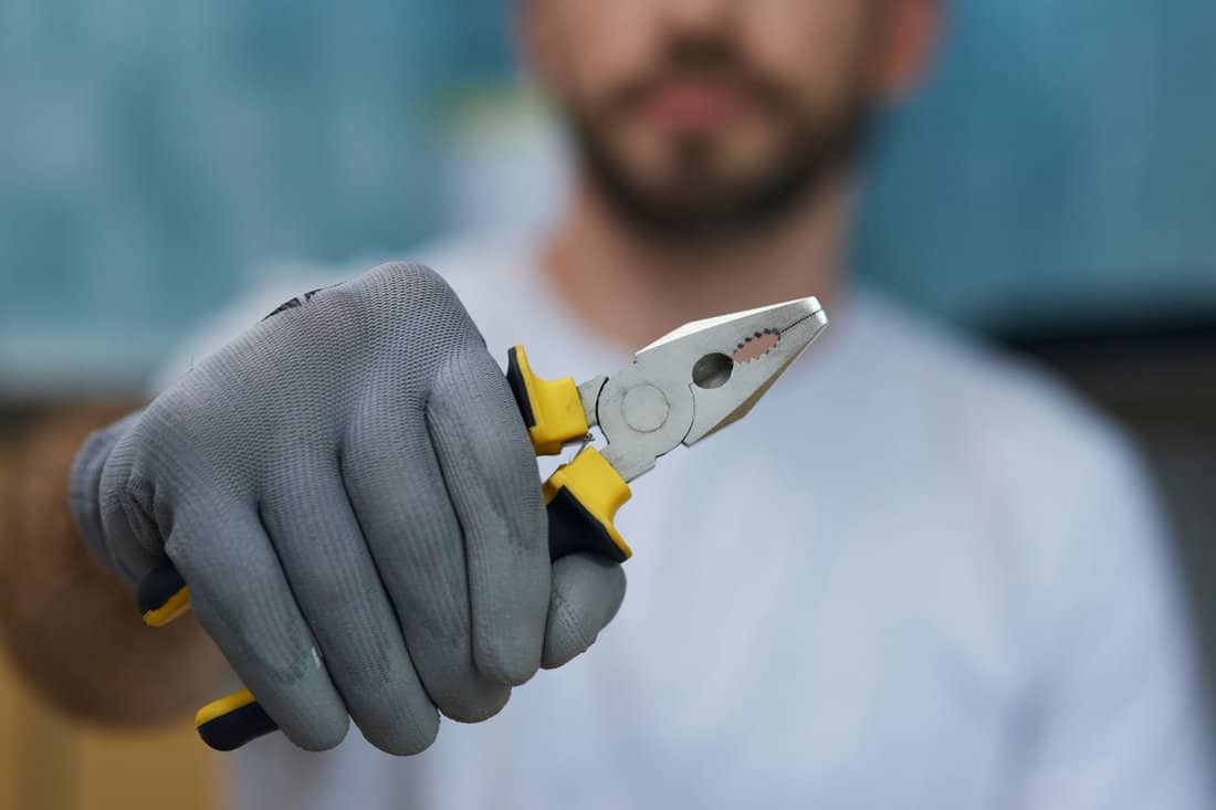 Pliers with insulated handlers. Close up shot of hand of young repairman holding pliers