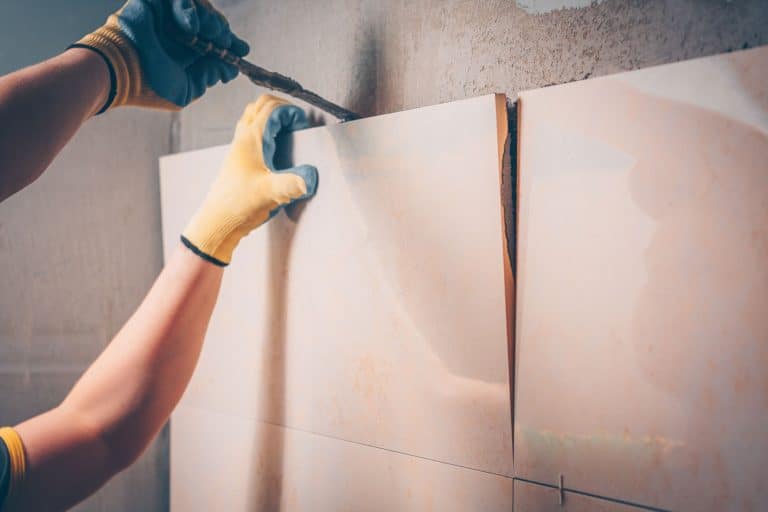 The working tiler removes the glued tile from the wall, the technology of professional and highly skilled tile work - How to Remove Mortar From Old Tiles For Reuse [the Ultimate Guide]