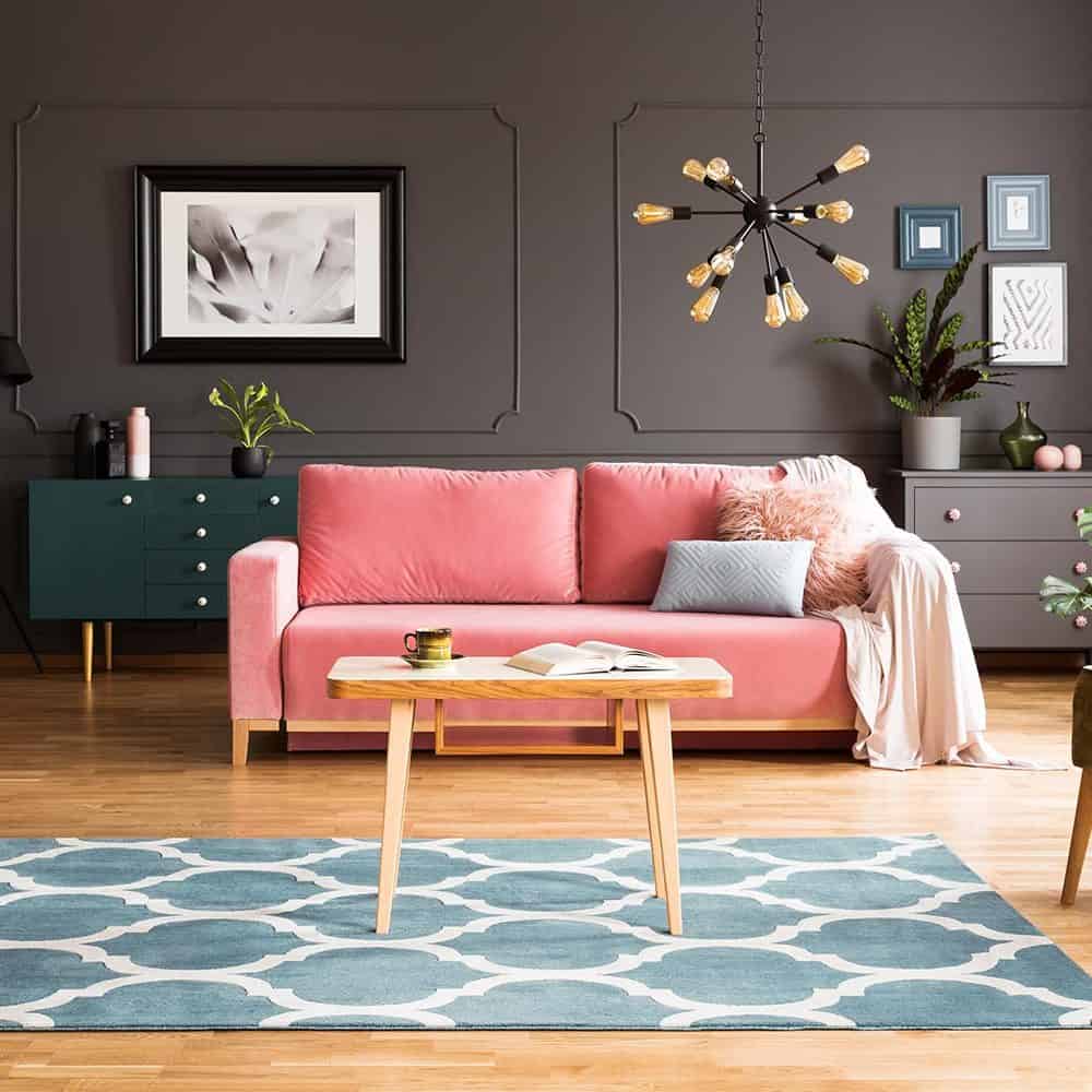 Wooden coffee table on blue rug over wooden flooring. Dark grey living room walls. coral pink sofa