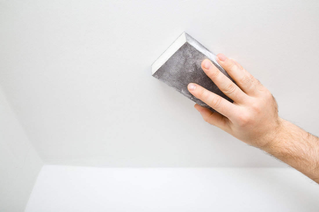 Worker hand polishing white ceiling with sanding sponge.