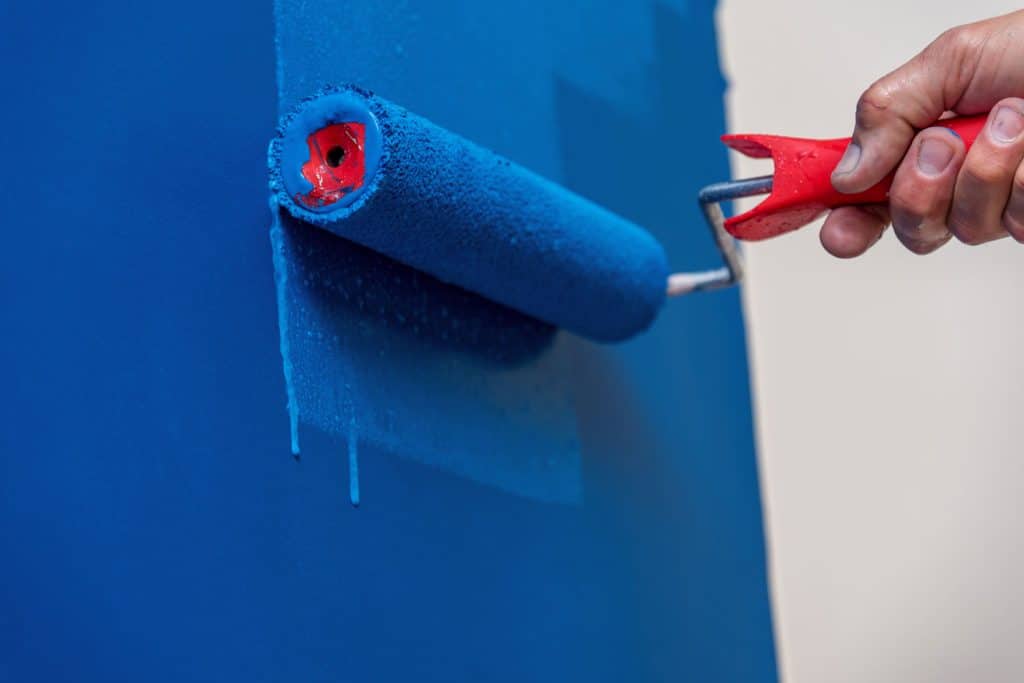 Painter using a roller to paint the wall with a blue color