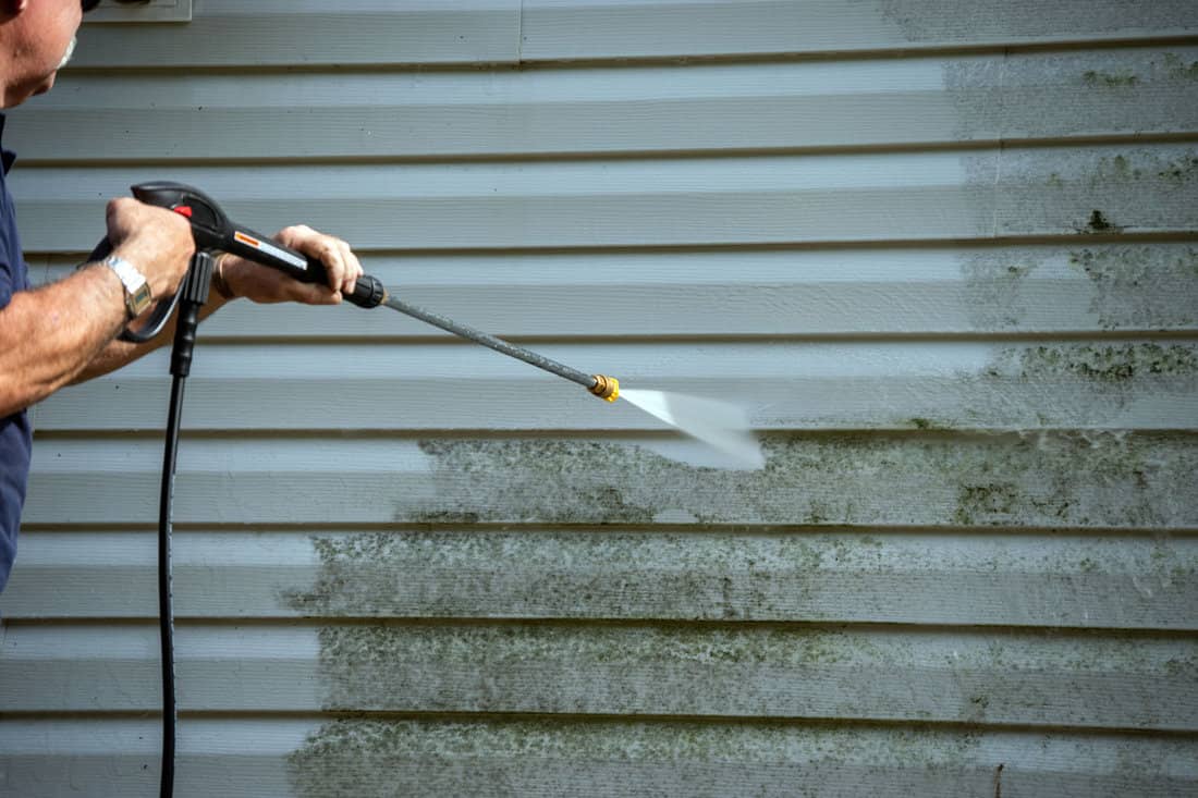 Worker using a power sprayer to clean the wall
