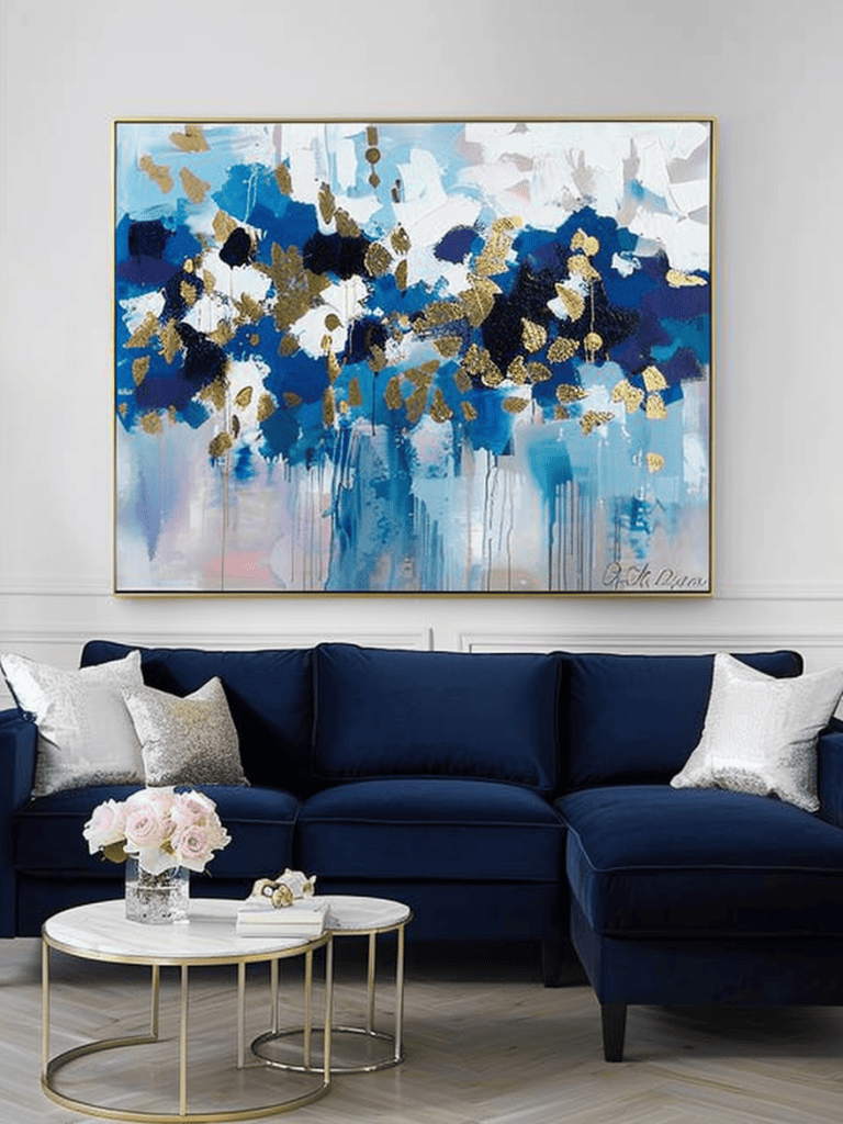 Luxurious contemporary living room. With crisp white walls, a navy blue velvet sectional sofa, and an oversized abstract painting with splashes of blue, white, and gold leaf. Complemented by a pair of round gold nesting coffee tables and a bouquet of soft pink roses in a clear glass vase ar 3:4