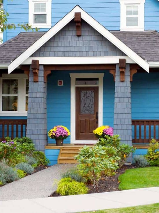 Blue walled front porch with brown door and garden on the side of the pathwalk