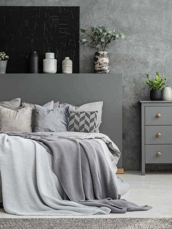 Monochromatic gray bedroom interior with a big bed with throw pillows and a drawer cabinet against a wall with a black canvas