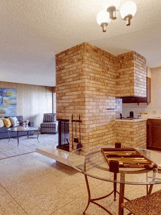 Rustic basement living room with dining and kitchen area separated with brick fireplace