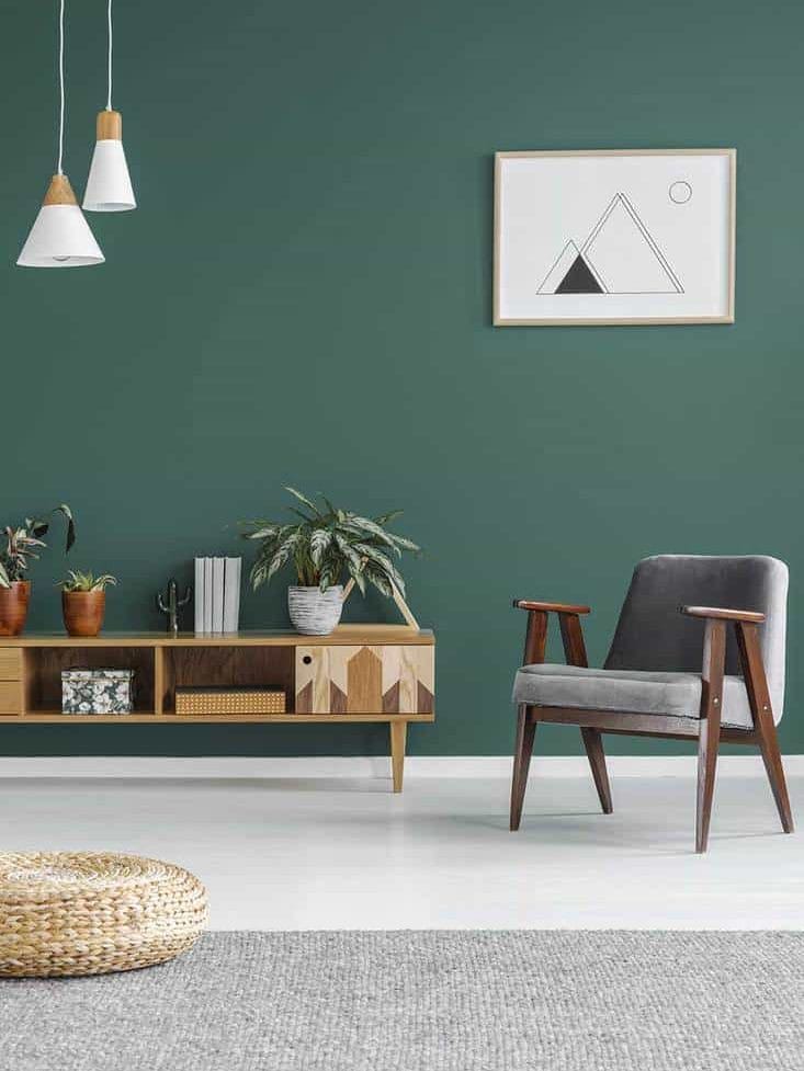 Simple geometric poster hanging on the wall in green living room interior with gray armchair, wooden cupboard and fresh plants