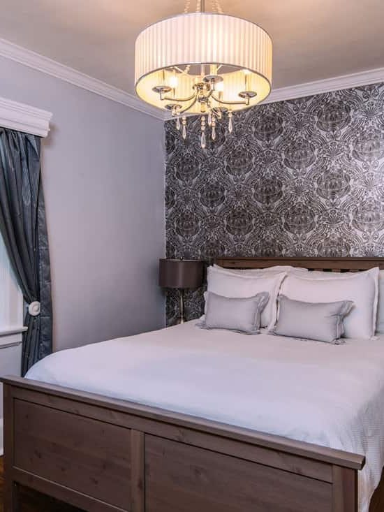 A gray wall with a floral patterned wallpaper and a white bedding set