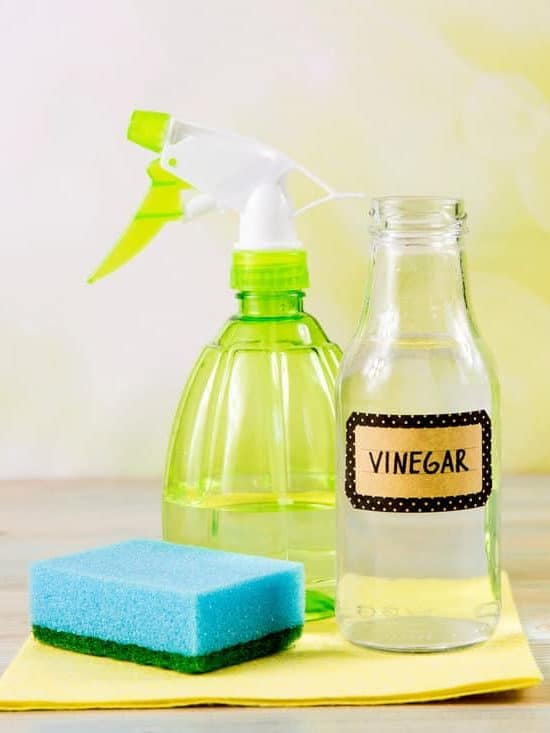 Chemical free home cleaner products concept. Using natural destilled white vinegar in spray bottle to remove stains. Tools on wooden table, green bokeh background, copy space. 