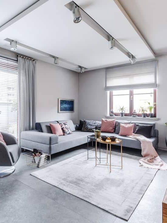Modern interior with large gray corner sofa and armchair decorated with pillows and blankets in a bright cosy living movie room with light from big glass door to balcony, wooden elements and decorations