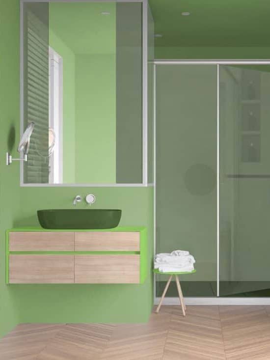 Minimalist bathroom in green tones with sink, large shower with glass cabin, heated tower rail with towels, herringbone parquet, window with venetian blinds. 