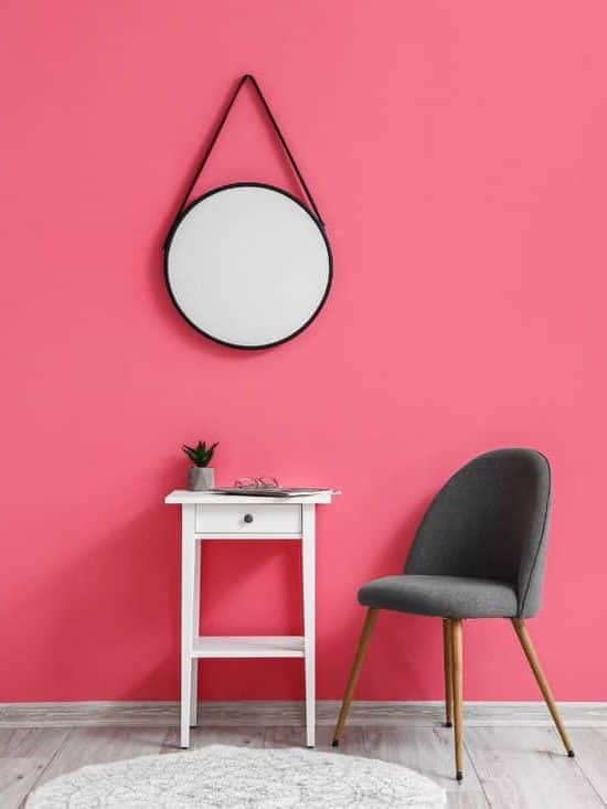 Modern chair with table and mirror near pink wall.