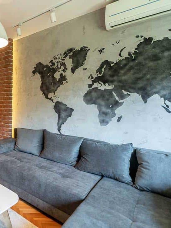 Modern living room interior with world map on the wall, cozy grey sofa, parquet floor and TV hang on brick wall