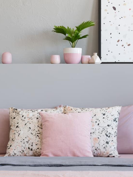 Pink and patterned pillows on bed with headboard in grey bedroom interior 